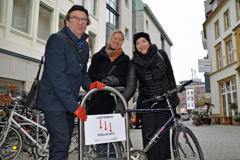 Haben das neue „Lastenradstellplatz“-Hinweisschild nahe der künftigen Fahrradabstellanlage bei P&C am Kamp angebracht: (V.l.) Stadtbaurat Frank Otte, Projektpatin Susanne Hambürger dos Reis und „Mobile Zukunft“-Projektleiterin Brigitte Strathmann
