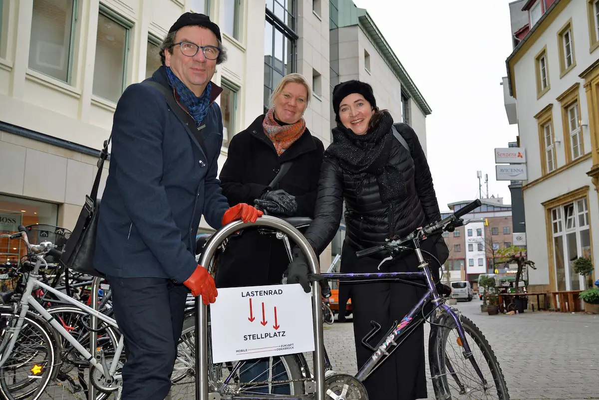 Haben das neue „Lastenradstellplatz“-Hinweisschild nahe der künftigen Fahrradabstellanlage bei P&C am Kamp angebracht: (V.l.) Stadtbaurat Frank Otte, Projektpatin Susanne Hambürger dos Reis und „Mobile Zukunft“-Projektleiterin Brigitte Strathmann