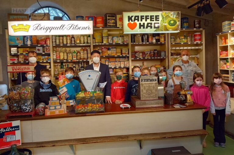 Jan Tönnies (hinten links), Nils-Arne Kässens und Dr. Thorsten Heese stehen mit 4. Klässlern der Grundschule Eye im Tante-Emma-Laden. / Foto: Brockfeld