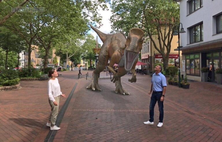 Neben den 25 lebensgroßen Dino-Figuren bevölkern auch zehn virtuelle Dinos auf Basis der Augmented-Reality-Technik die Oeseder Innenstadt. Mit dem Cryolophosaurus haben das Doreen Wolter und Olaf Bick auf dem Roten Platz schon einmal ausprobiert. / Foto: Stadtmarketingverein Georgsmarienhütte
