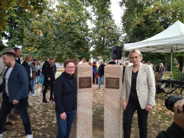 Diana Häs (Vorstandsvorsitzende Gay in May) und Oberbürgermeisterin Katharina Pötter stehen neben dem Mahnmal gegen Homophobie und für Zivilcourage. / Foto: Julian Tischer