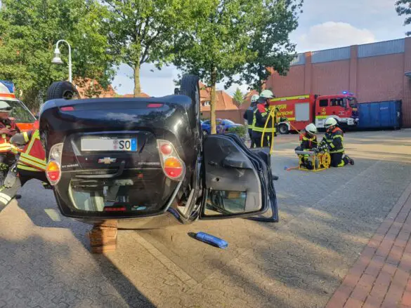 PKW auf dem Dach, Ansicht Heck, Feuerwehrleute im Hintergrund