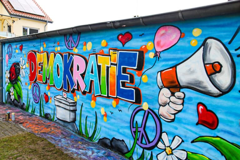 Bunt und mit Botschaft: In Großbuchstaben ziert das Wort „Demokratie“ nun die Rückwände von einigen Garagen unmittelbar am Spielplatzgelände. in Landkreis Osnabrück (Region)