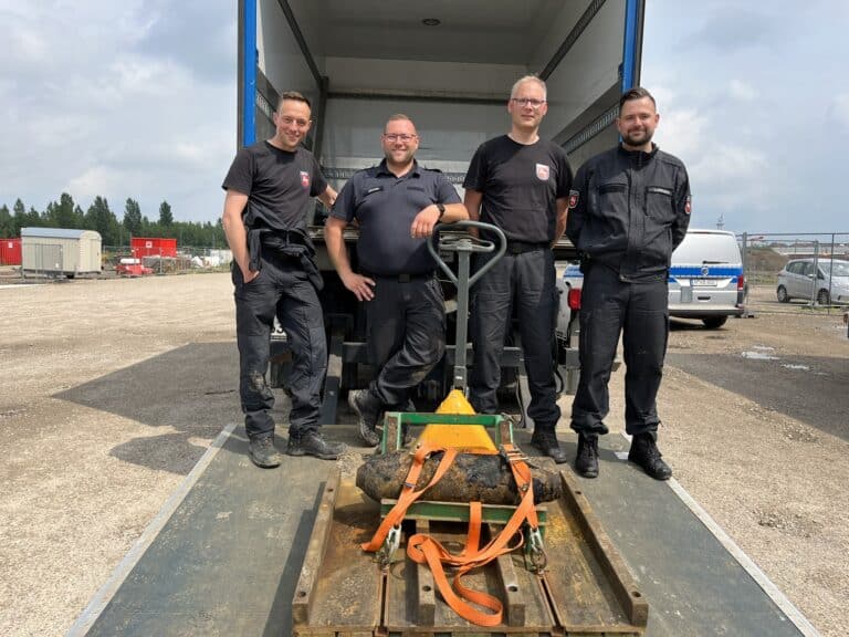Sprengmeister Christoph Coldewey und seine Kollegen Lukas Ahrens, Hinrich Brand und Dominik Luttmann (von links) präsentieren eine der beiden amerikanischen 100-lbs-Bomben, die sie am 31. Mai 2026 im Lokviertel unschädlich gemacht haben. Den zweiten Blindgänger musste der Kampfmittelbeseitigungsdienst sprengen. / Foto: Constantin Binder
