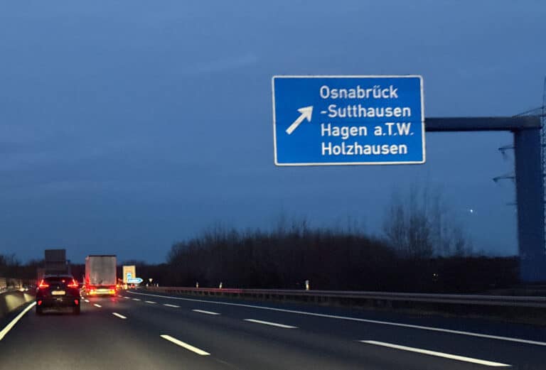 Wegweiser zur Abfahrt Osnabrück-Sutthausen über der Autobahn A30 in der Dämmerung