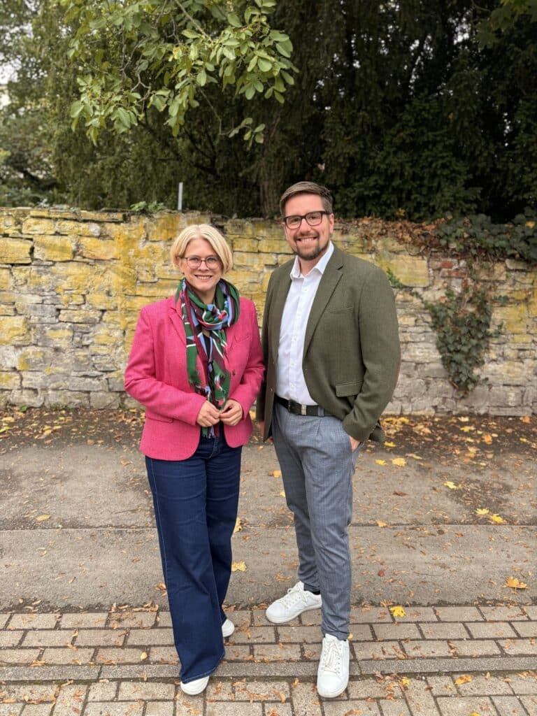 Verena Kämmerling (links) und Christopher Peiler stehen nebeneinander vor einer bewachsenen Bruchsteinmauer