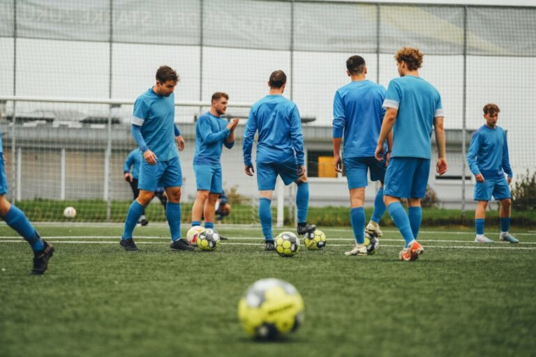 Amateurfußballer in hellblauen Trainingstrikots beim lockeren Aufwärmen mit Bällen auf einem Kunstrasenplatz