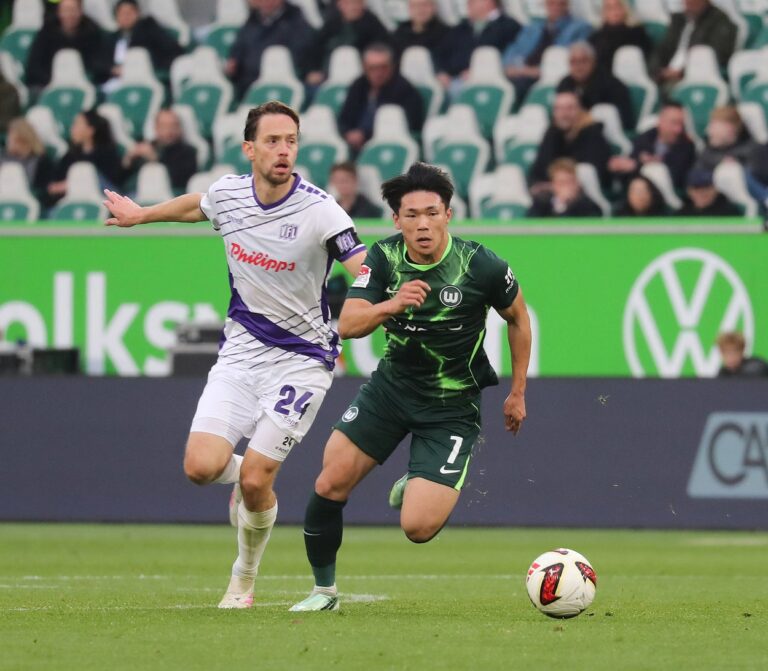 Zweikampf im Wolfsburger Stadion: Ein Spieler des VfL Osnabrück im weiß-lila Trikot und ein Wolfsburger Spieler im grünen Trikot laufen dem Ball hinterher. Foto: IMAGO / Susanne Hübner