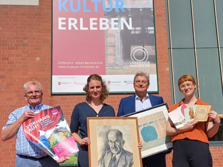 Vor dem acht Meter hohen Banner am Kreishaus werden Objekte rund um das Jubiläum des Bersenbrücker Museums präsentiert (von links): Kulturbüroleiter Burkhard Fromme mit einem Plakat für das Theater „Vorhang auf!“, Museumsleiterin Katharina Pfaff mit einem Portrait von Museumsgründer Rothert, Kreisrat Matthias Selle mit einem Aquarell Theodor Doebners und Museumspädagogin Claudia Stuckenberg mit Museumsführern aus drei Epochen. / Foto: Henning Müller-Detert