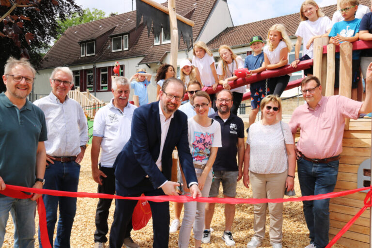 Zur Freigabe des neuen Spielgeländes schnitt Erster Stadtrat Alexander Herzberg mit Vertreterinnen und Vertretern aus Politik und Verwaltung, der Schulleitung sowie den Ortsbotschafterinnen und Ortsbotschaftern des Stadtteils Harderberg symbolisch ein rotes Band durch.