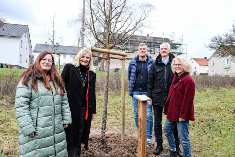 Bildunterschrift: Haben den neuen Apfelbaum auf der Grünfläche am Patkegarten in Holzhausen begutachtet: Gesche Wiggers (Klimaschutzmanagerin) und Bürgermeisterin Dagmar Bahlo gemeinsam mit den ROLLSHausen-Teammitgliedern Michael Langer, Frank Schlösser und Margit Spreckelmeyer. Foto: Stadt Georgsmarienhütte/ Niklas Otten