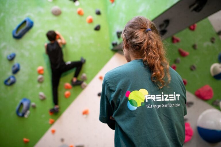 Deborah Berndt, Projektmitarbeiterin von Exil e.V., beobachtet ein Kind beim Klettern – das Projekt „FreiZeit für junge Geflüchtete“ schenkt jungen Bewohner*innen der Erstaufnahme Bewegung, Begegnung und Selbstvertrauen. / Foto: Nds. Lotto-Sport-Stiftung/Johannes Krüger