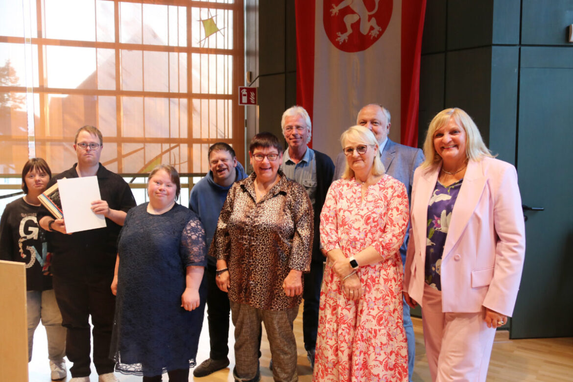 Gemeinsam auf der Bühne: Mit den Bewohnerinnen und Bewohnern der Wohngruppe „Mittendrin“ nahmen die Beteiligten die Ehrengabe aus den Händen von Bürgermeisterin Dagmar Bahlo entgegen. / Foto: Niklas Otten